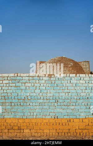 Rough weathered colorful painted brick wall located on street of town with old building against cloudless blue sky in Egypt Stock Photo