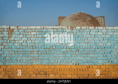 Rough weathered colorful painted brick wall located on street of town with old building against cloudless blue sky in Egypt Stock Photo