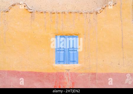 Full frame facade of weathered yellow painted house with shabby wall and small blue windows located on street in town Stock Photo