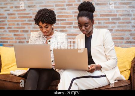 Positive African Americans female colleagues in elegant wear browsing netbooks while working on project together on couch in light modern office Stock Photo