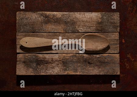 Top view of big old fashioned wooden spoon placed on shabby chopping board made of wood on table in light kitchen at home Stock Photo