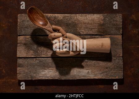 Top view of artificial mannequin hand with big wooden spoon placed on weathered cutting board on table in light room Stock Photo