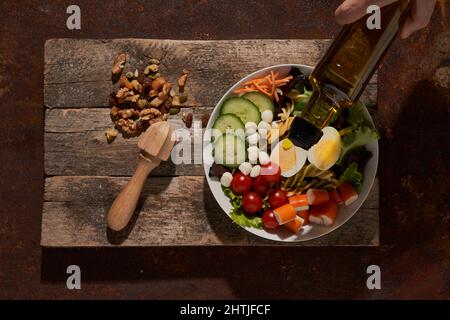 Top view of fresh salad with vegetables and eggs placed on rusty table near lemon reamer on cutting board Stock Photo