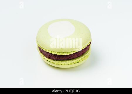 From above one sweet round green macaroon with white spot and tasty chocolate filling placed on white background in light room Stock Photo