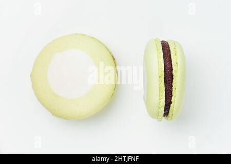 From above sweet round green macaroons with white spots and tasty chocolate filling placed on white background in light room Stock Photo