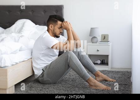 Life Troubles. Depressed Pensive Young Arab Man Sitting On Floor Near Bed Stock Photo