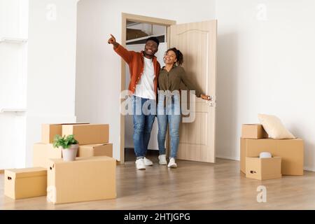 Excited Black Spouses Entering Their New Home, Husband Pointing Aside Stock Photo