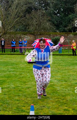 Christchurch, Dorset, UK. 1st March, 2022. Drizzle on pancakes! Flipping good fun had by all at Christchurch pancake race in Dorset on Shrove Tuesday on a drizzly morning - the miserable weather didn't deter those taking part and having fun. Credit: Carolyn Jenkins/Alamy Live News Stock Photo