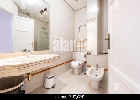 Bathroom with cream marble vanity and white porcelain sink with frameless square glass mirror and matching white porcelain fixtures in vacation rental Stock Photo