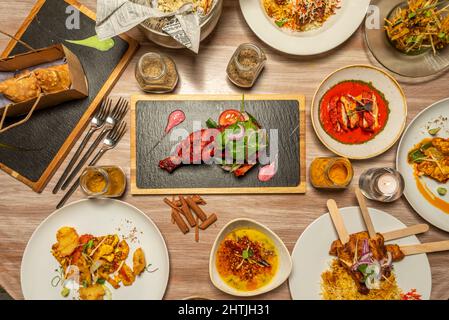 Set of Indian food dishes with chicken tikka masala in the center, meat stuffed samosas, red curry, korma, cinnamon sticks, pilau rice and more spices Stock Photo