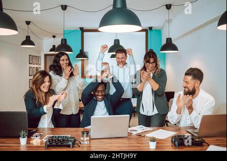 Multiracial coworkers celebrating victory at table Stock Photo