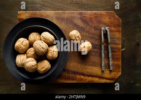 Walnuts in a black bowl and old nutcracker on a vintage cutting board, Italy, Europe Stock Photo