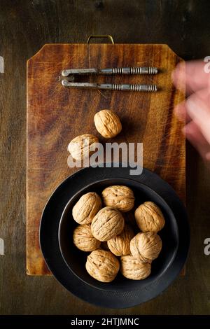 Walnuts in a black bowl and old nutcracker on a vintage cutting board, Italy, Europe Stock Photo