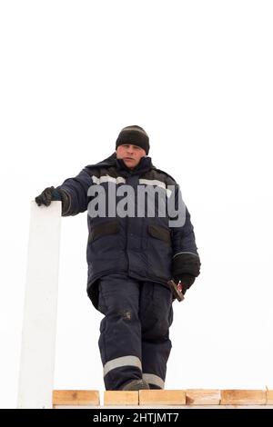 Builder in a blue jacket with a hood with a board in his hand on the installation of a wooden slide Stock Photo