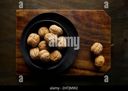 Walnuts in a black bowl on a vintage cutting board, Italy, Europe Stock Photo