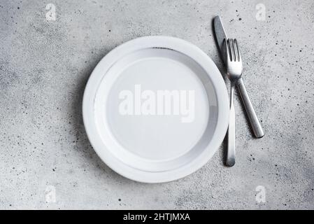 Empty plate and silver cutlery on grey concrete background, top view copy space. Table setting Stock Photo