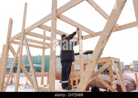 A builder in a blue jacket with a hammer in his hand hammers a nail Stock Photo