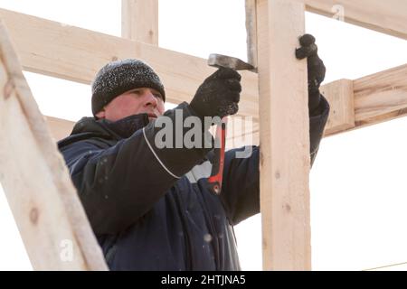 A builder in a blue jacket with a hammer in his hand hammers a nail Stock Photo