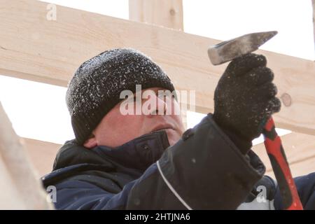 A builder in a blue jacket with a hammer in his hand hammers a nail Stock Photo