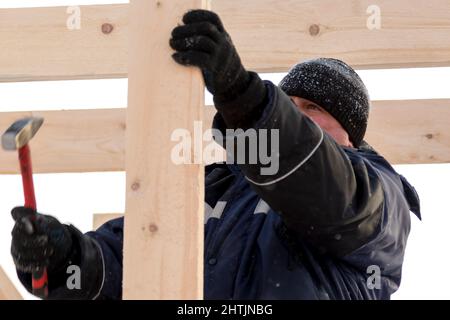 A builder in a blue jacket with a hammer in his hand hammers a nail Stock Photo