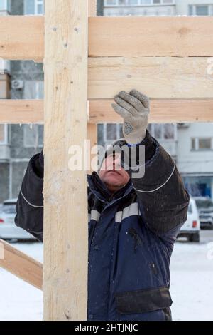 A builder in a blue jacket with a hammer in his hand hammers a nail Stock Photo