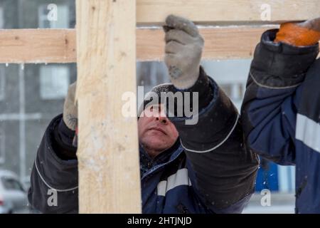 A builder in a blue jacket with a hammer in his hand hammers a nail Stock Photo