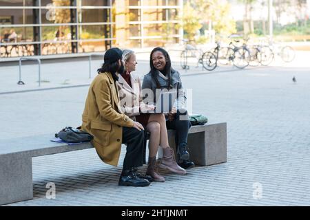 Business people using a laptop together while discussing new business projects sitting on a bench on the street. Stock Photo