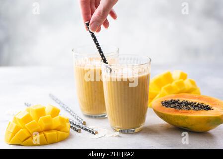 Tropical Mango Papaya Smoothie In Glass. Healthy vegetarian fruit drink in glass with paper drinking straw Stock Photo
