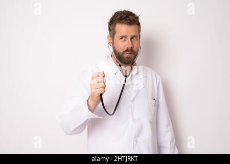 Laughing funny young bearded doctor man wearing white medical gown standing hold stethoscope isolated on white background. Medicine concept. Stock Photo