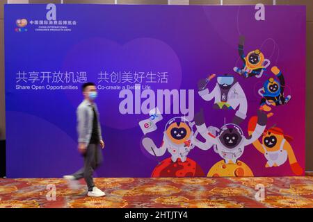 (220301) -- HAIKOU, March 1, 2022 (Xinhua) -- A visitor walks past a billboard showing the images of the mascots for the 2022 China International Consumer Products Expo, styled after the Hainan gibbon, in Haikou, south China's Hainan Province, March 1, 2022. Hainan gibbons are the most endangered of all gibbons and the world's rarest primate. They are endemic to the southern Chinese island of Hainan. The mascots reflect the green consumption approach of the expo, according to Ruslan Tulenov, a global media officer at the Hainan Provincial Bureau of International Economic Development. The mas Stock Photo