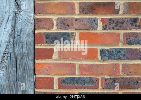 Close up section of mixed red brick wall, stretcher bond format with vertical wooden beam running through Stock Photo