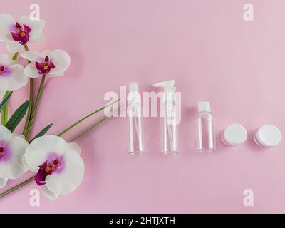 Empty plastic beauty bottles on a pink background with realistic fake orchids on the left.  Flat Lay. Copy Space. Stock Photo