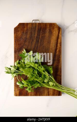 Mediterranean ingredients, fresh parsley from Southern Italy on an old wooden cutting board and a white marble background, Italy, Europe Stock Photo