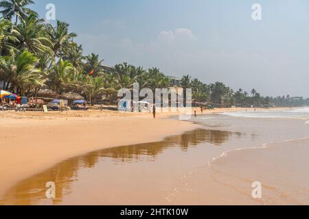 HIKKADUWA, SRI LANKA - JANUARY 22, 2022: Narigama beach at Hikkaduwa with people walking along the coastline with palmtrees Stock Photo