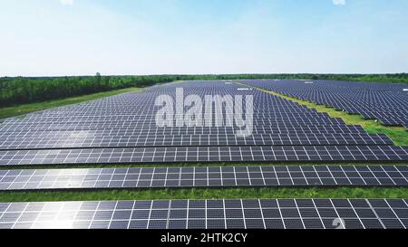 beautiful aerial view of solar panels on solar farm during a sunny day with plants and sky in the background. Stock Photo