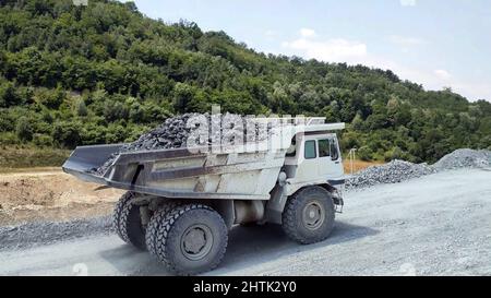 white Haul truck truck load of gravel rocks in the quarry from side view, big and large articulated dumping truck, dumper trailer, dump lorry. Stock Photo