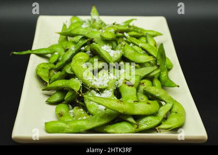 Portion of green Edamame cooked and salted ready to eat, healthy japanese appetizer on a black background. Stock Photo