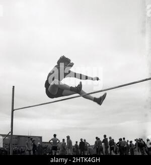 1960s, historical, school sports, a teenage boy in shorts and pilmsolls doing the high jump, using his own technique, Scotland, UK.