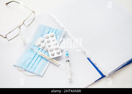 Medical background: pills, glasses, pen, mask, thermometer, vaccine, syringe and papers with patient data. Medical theme. Concept: vaccination against Stock Photo