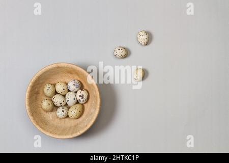 Quail eggs in a wooden bowl and on a gray background in a top view Stock Photo