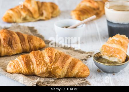 Delicious French croissant on a white wooden table, a cup of coffee and croissants in the background, breakfast scene Stock Photo