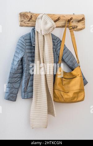 Natural wooden coatrack with jacket, scarf and bag on a white wall. Scandinavian interior style. Stock Photo