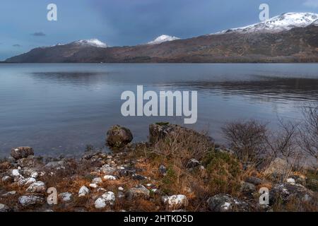 LOCH MAREE KINLOCHEWE SCOTLAND  STONES WITH WHITE LICHENS SNOW ON THE HILLS WHITE HOUSE AT FURNACE Stock Photo