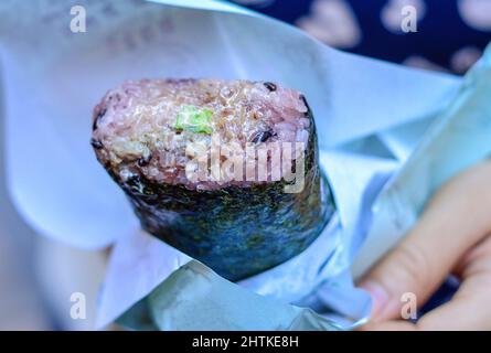 Hand holding a big Japanese sushi hand roll with seaweed outside, meat, vegetable and rice inside. Stock Photo