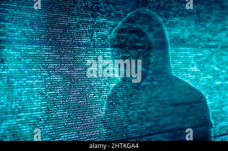 The silhouette of a hacker in front of program code Stock Photo
