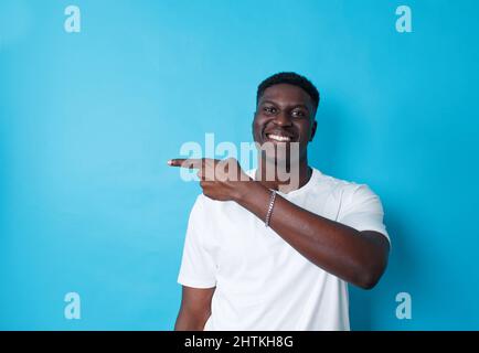 African-American pointing the side with his finger on an isolated blue background Stock Photo