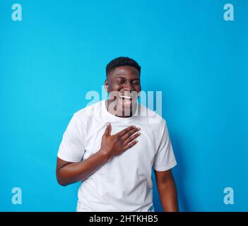 A young African-American man in a white T-shirt laughs on a blue isolated background Stock Photo