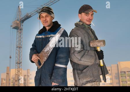 Two bad unskilled builder workers in bad dirty tattered uniform with bad tools. Concept of unskilled workers or crooks or poor quality workers Stock Photo
