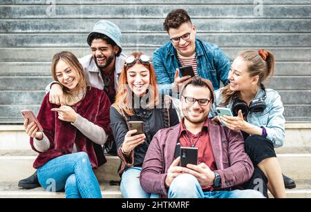 Multicultural urban friends having fun on mobile phone at urban place - Young happy guys and girls sharing time together watching funny video on smart Stock Photo