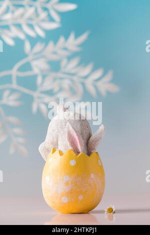 A white rabbit hid in an Easter egg on a blue background. Festive Easter card. Stock Photo